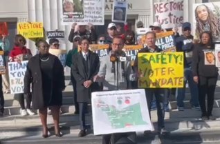 Shane Reisman at a public advocacy event, standing among speakers and supporters with a California map visible at the podium.